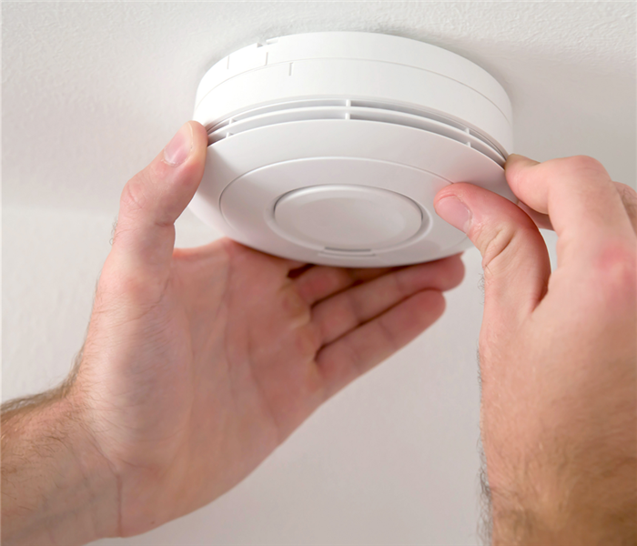 two hands around a smoke alarm on the ceiling 