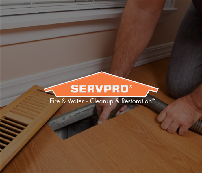 Man kneeling with a tube down into the air ducts with Servpro logo over the photo